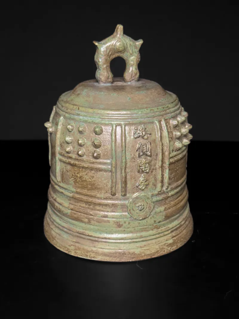 Bronze-toned ceramic bell with raised studs and characters
